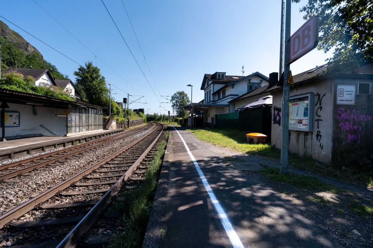 Bahnhof Erpel mit Gleisen, einem Bahnsteig, einem Weg und einem "DB"-Schild an einem sonnigen Tag.