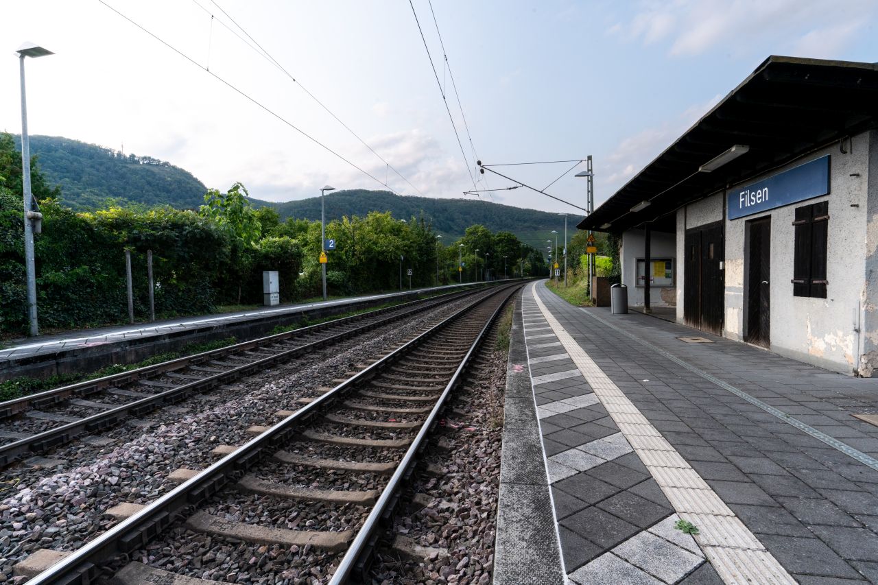Bahnhof Filsen mit zwei Gleisen, einem Bahnsteig und einem Unterstand vor grünen Hügeln und Bäumen.