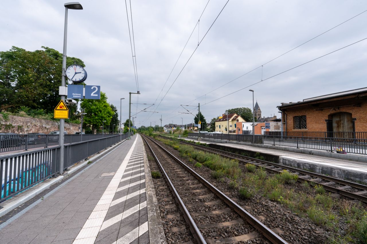 Leerer Bahnsteig des Bahnhof Geisenheim mit Gleisen und einer Uhr unter einem bewölkten Himmel.