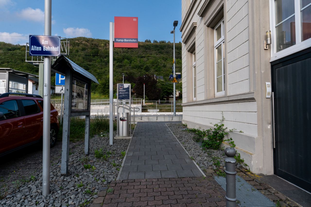 Ein Weg mit einem roten Schild und einem blauen Straßenschild "Am Alten Bahnhof" führt zum Bahnsteig des Bahnhof Kamp Bornhofen.