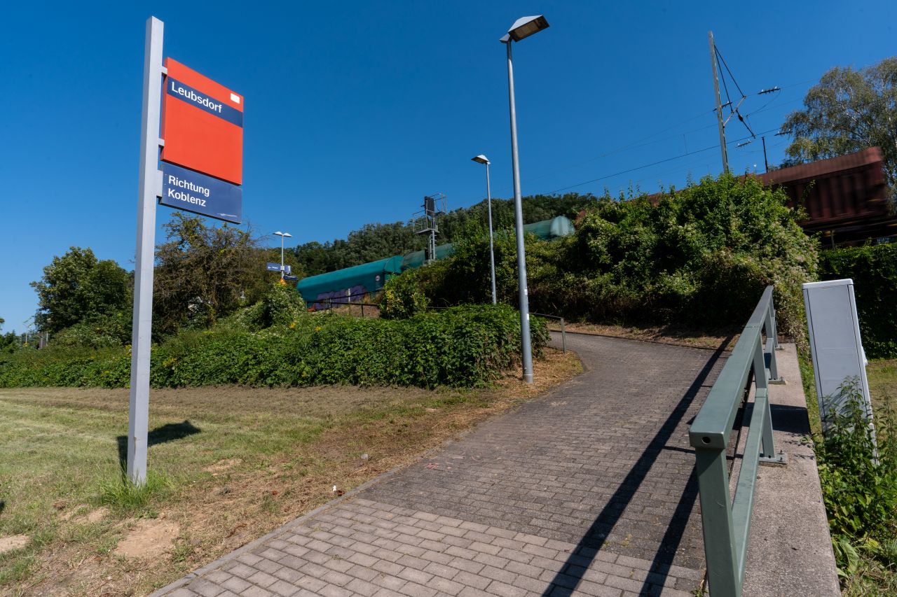 Ein steiler Weg mit einem Schild "Leubsdorf" führt zum Bahnsteig, der von einem Güterzug passiert wird.
