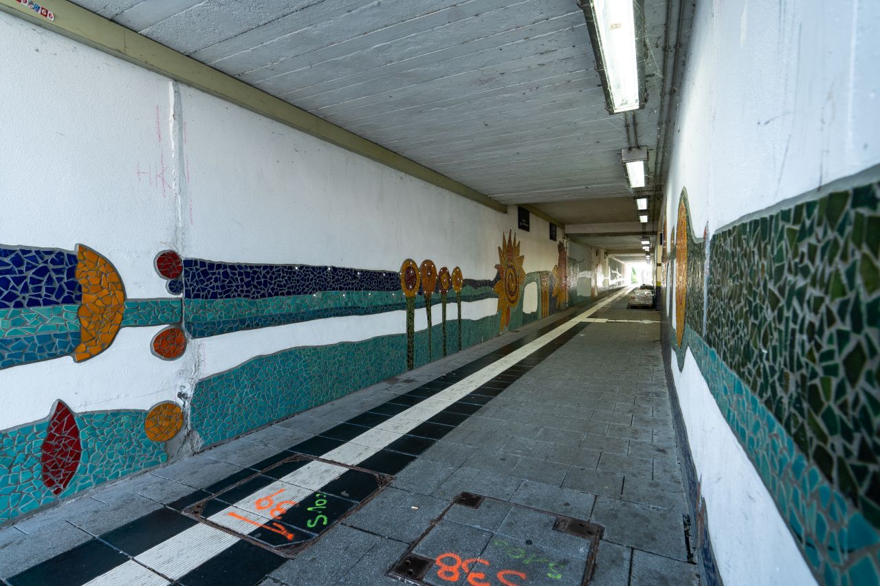 Fußgängertunnel mit bunten Mosaik-Kunstwerken an den Wänden, der zu den Steigen des Bahnhof Niederlahnstein führt.