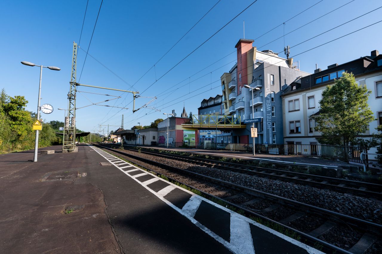 Station Oberlahnstein mit zwei Gleisen und einem Bahnsteig, mit Blick auf farbige Gebäude.