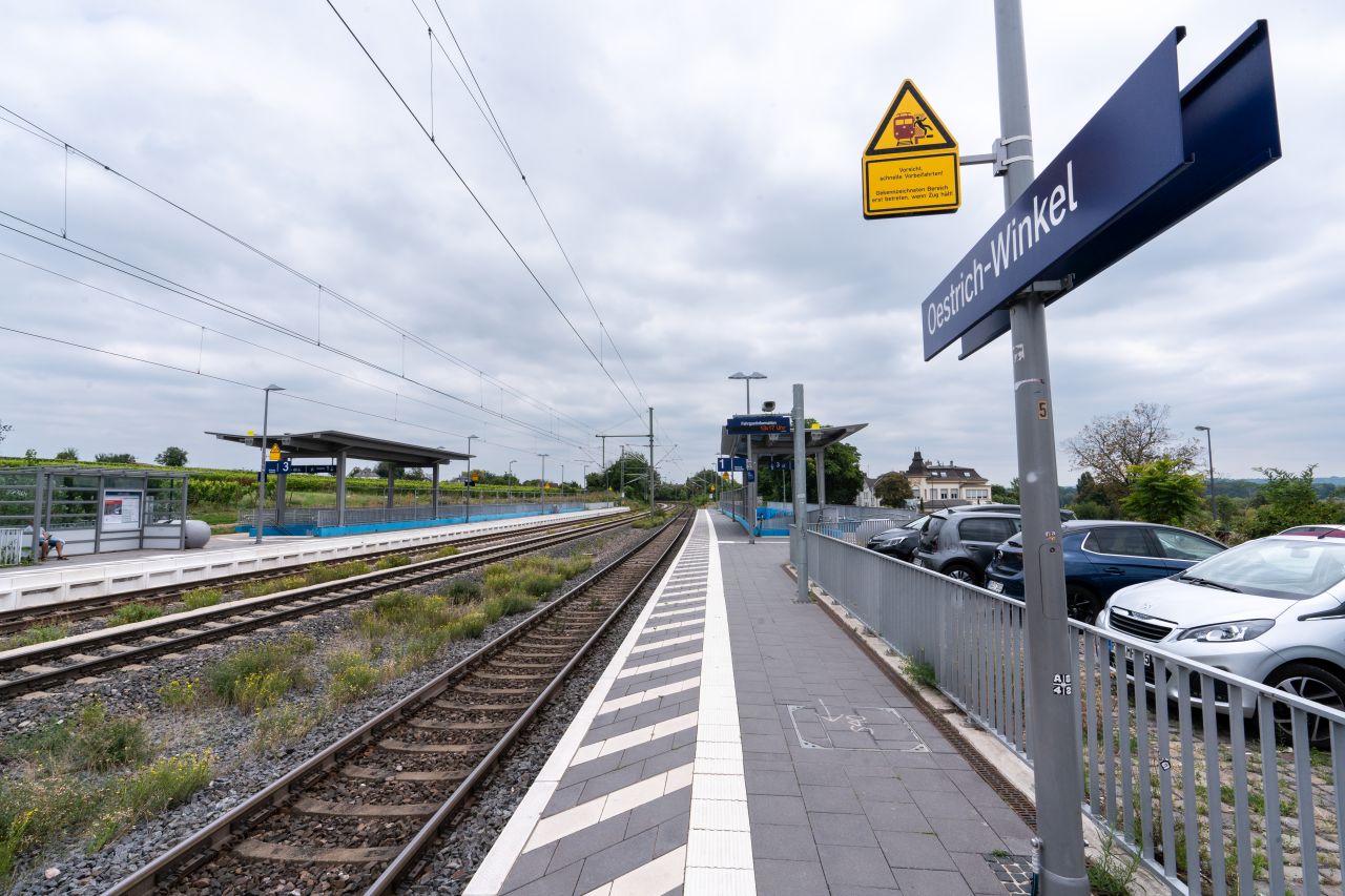 Bahnsteig der Station Oestrich-Winkel, der durch ein Geländer von einer nebenstehenden Parkmöglichkeit getrennt ist.