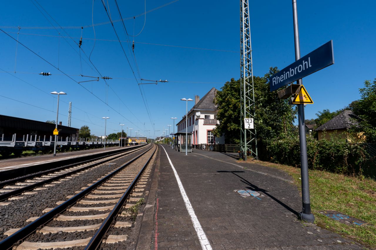Bahnsteig Rheinbrohl mit einem Schild, das den Namen Bahnhofs trägt sowie dem Bahnhofsgebäude auf der rechten Seite.