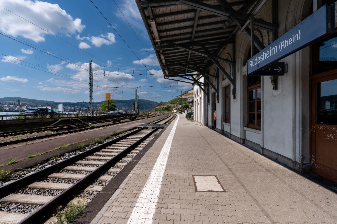 Leerer Bahnsteig am Bahnhof Rüdesheim (Rhein), von dem sich links eine Landstraße sowie ein Fluss befindet.