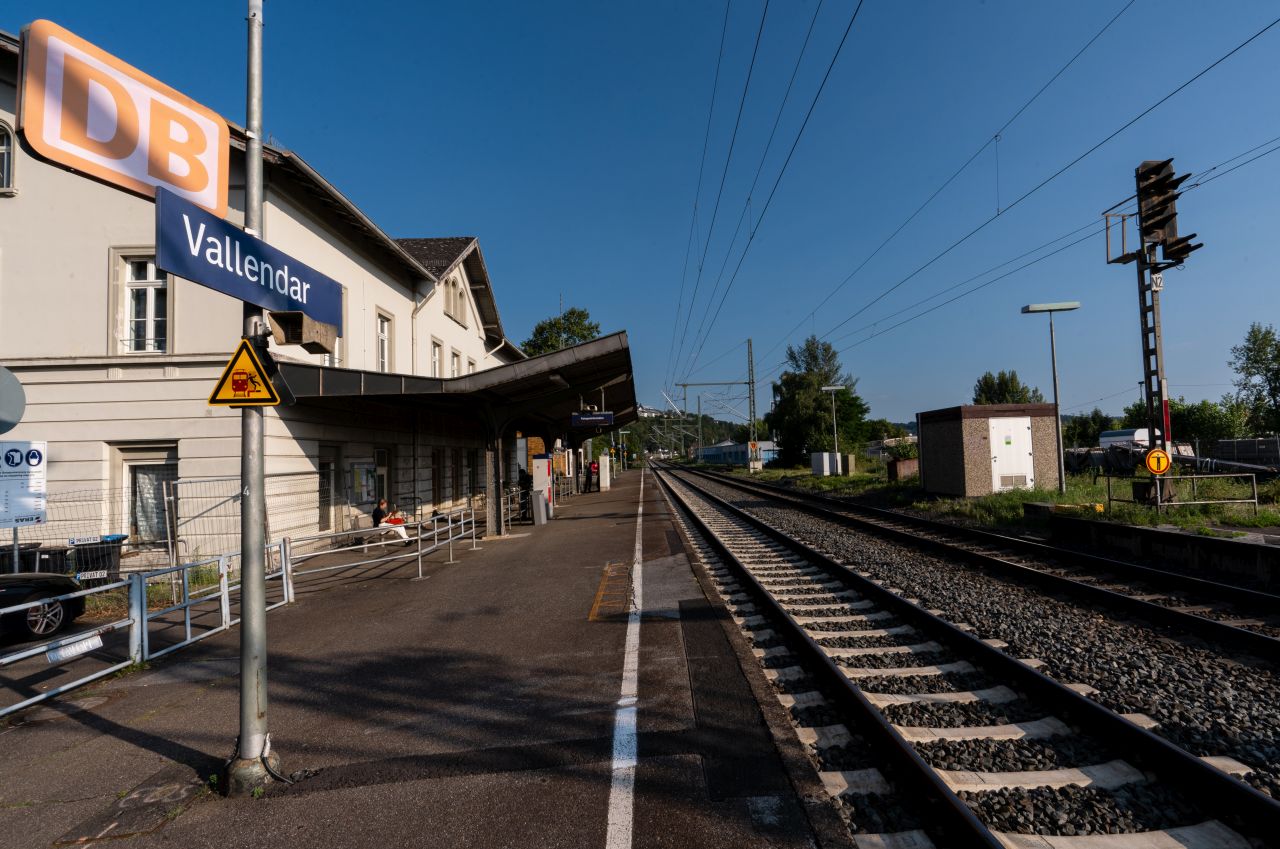 Bahnsteig mit Unterstand und Bahnhofsgebäude der Station Vallendar an einem sonnigen Tag.